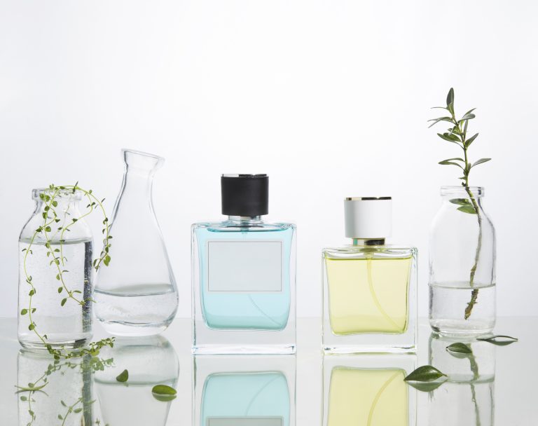 Perfume bottles and vases with fresh branches and flowers on a glass background